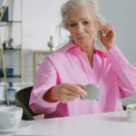 Starsza kobieta zakładająca aparat słuchowy przed lustrem w domu